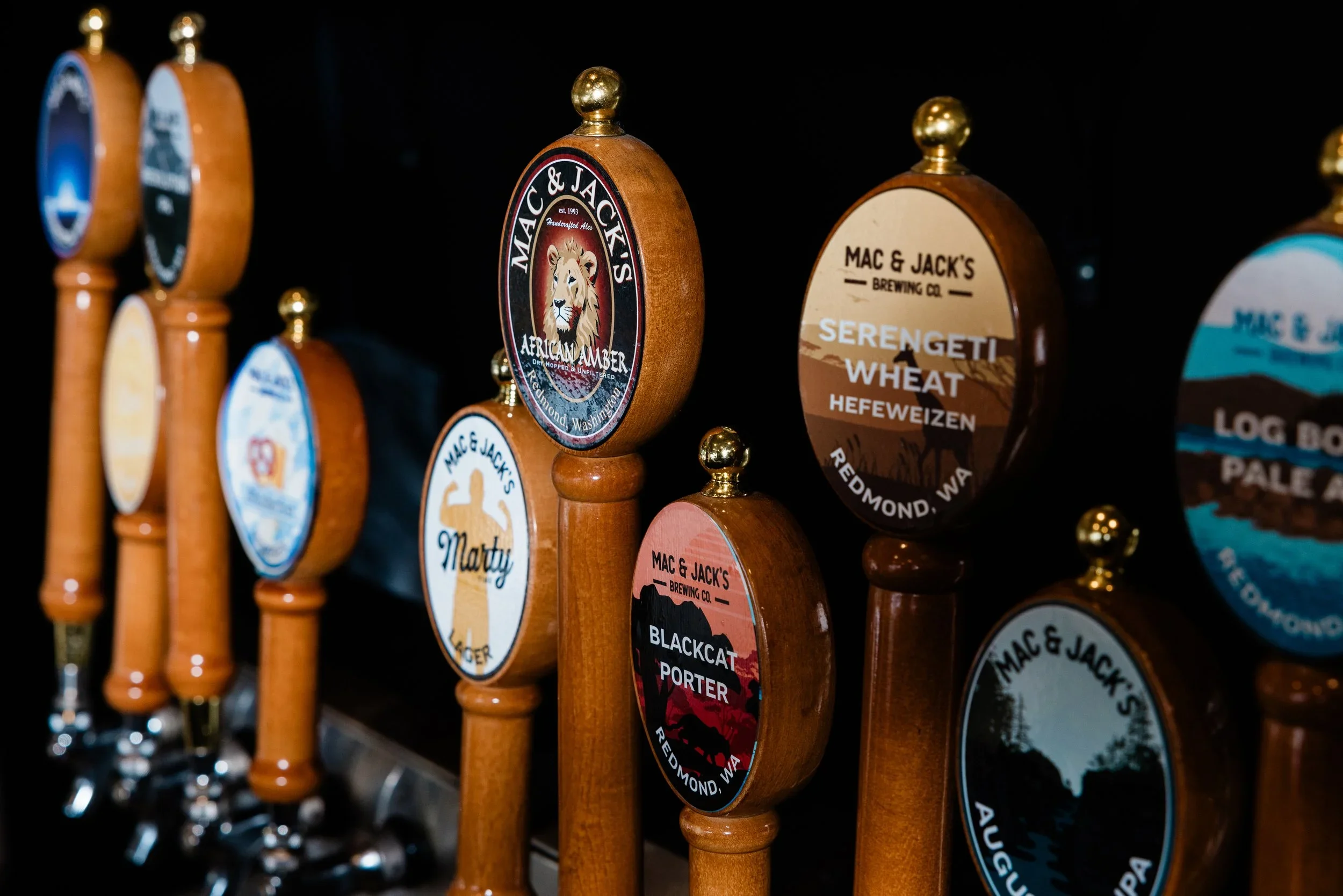 Rows of craft beer tap handles with colorful labels from Mac & Jack's Brewing Co.