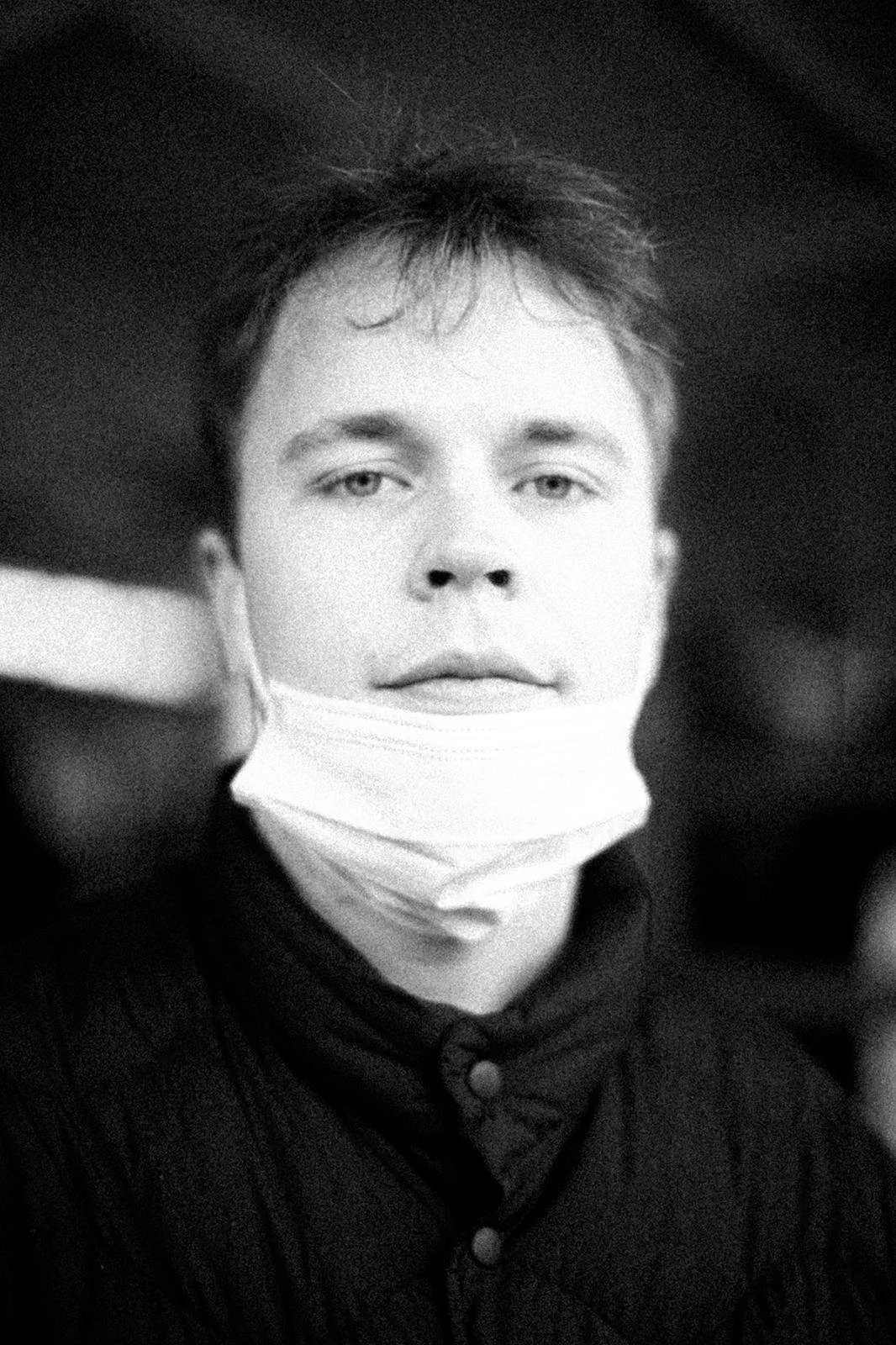 A young person with short hair wearing a face mask pulled down below their chin, looking directly at the camera.