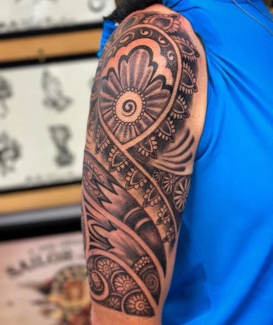 Close-up of a person's upper arm tattoo featuring a large spiral with floral and geometric patterns in black ink.