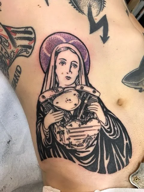 Tattoo of a religious figure holding an industrial machine on the person's side.