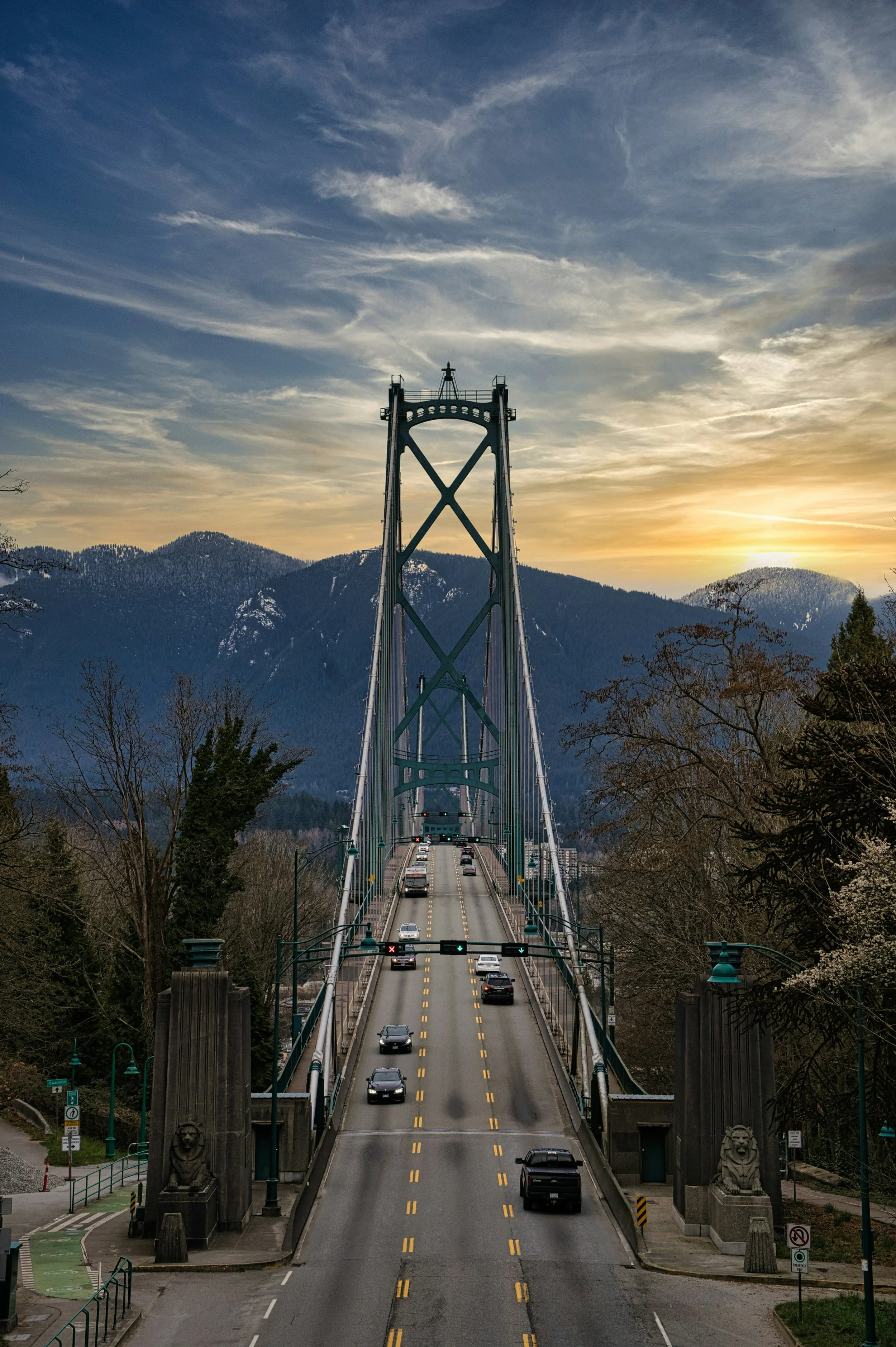 A bridge with a tower structure and cars crossing it at sunset, with mountains in the background.