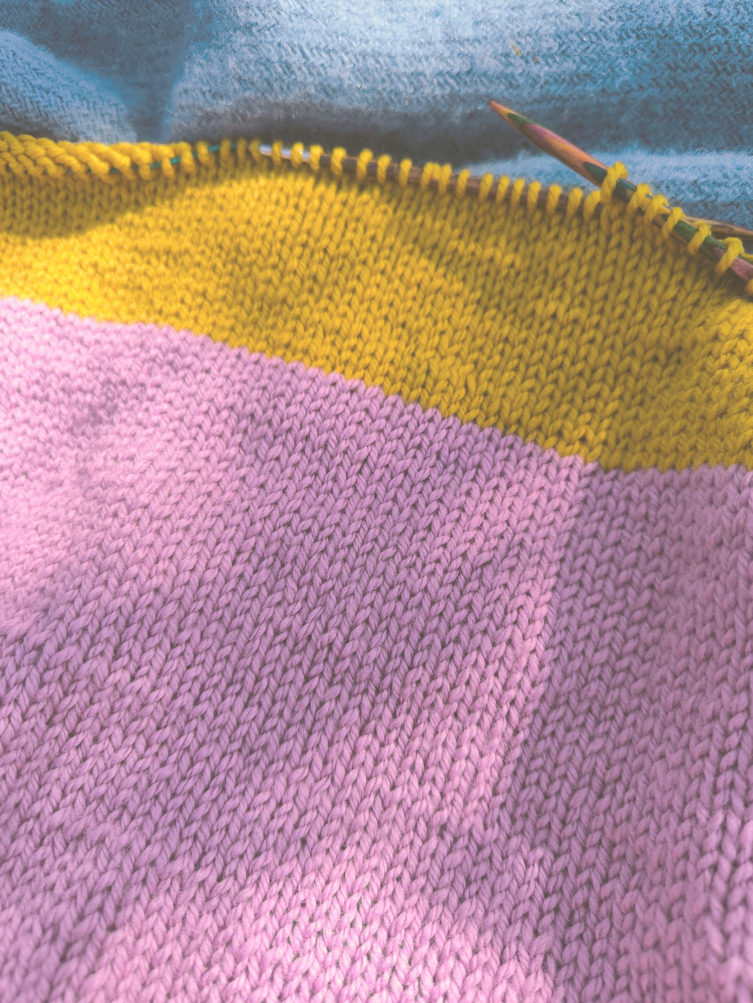 Nahaufnahme eines gestrickten Stoffes mit pink und gelber Farbe und einer Nadel