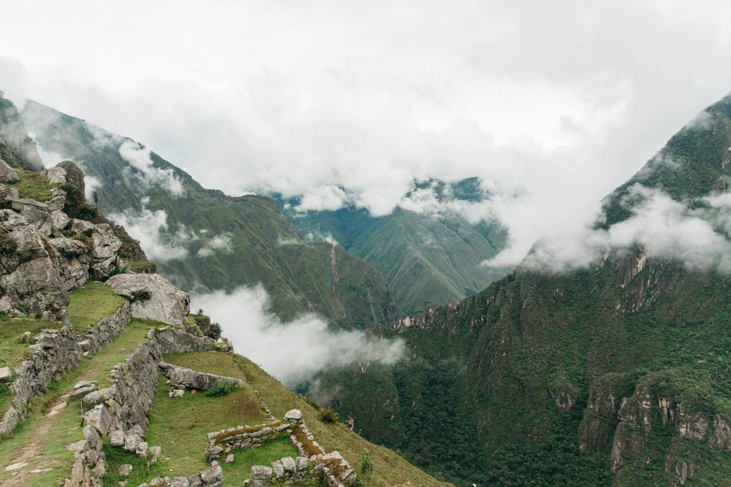 Auf dem Bild sind grüne Steilwände der Berge mit Wolken und Nebel bedeckt, dazu Terrassenfelsen und eine schmale Treppe im Vordergrund.