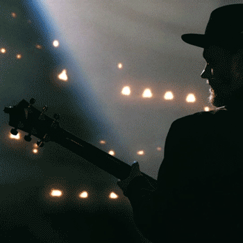 Silhouette of a Cas Haley, playing an electric guitar on stage with stage lights and fog in the background.