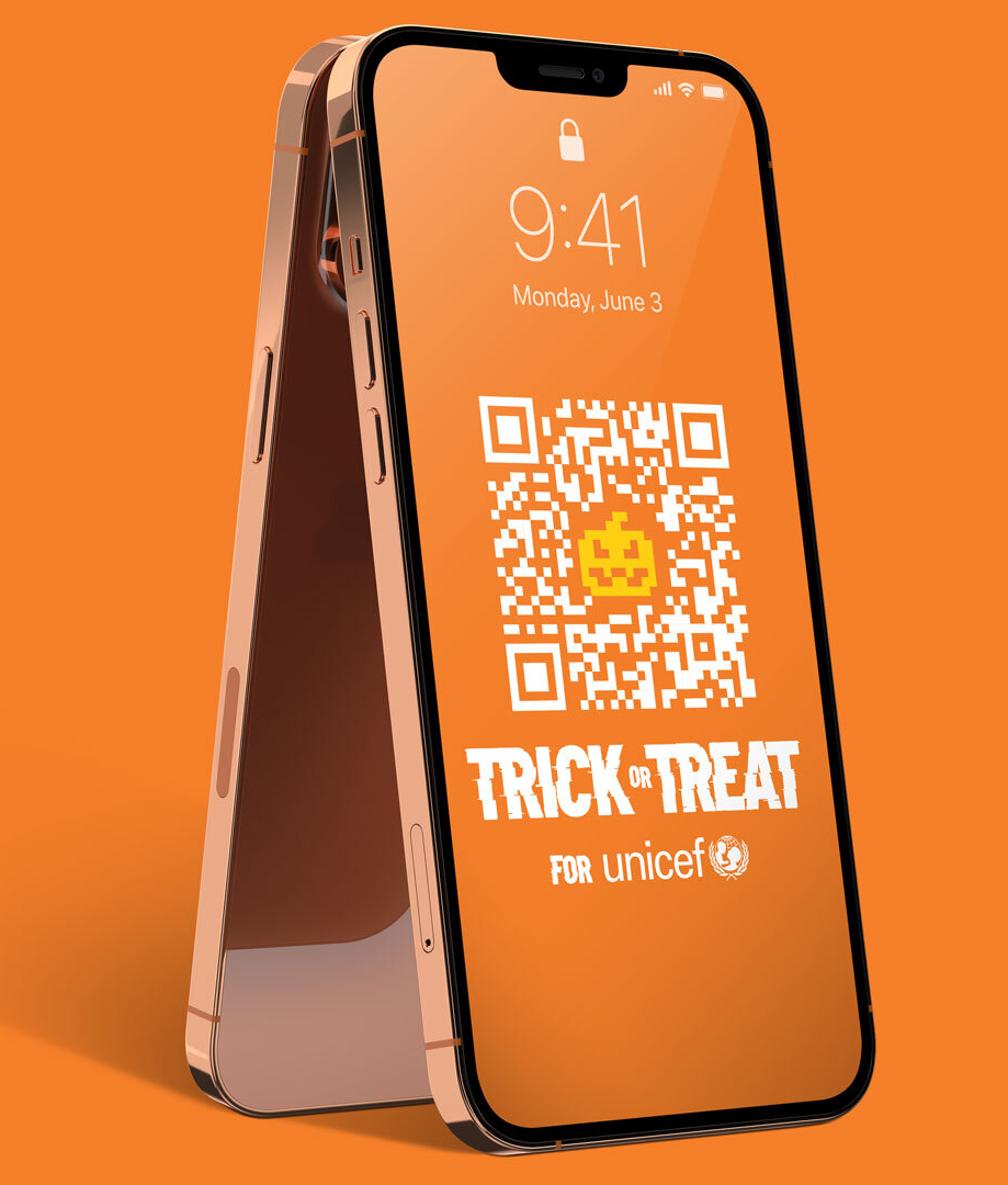 An iPhone with an orange background displaying a QR code for a Halloween-themed charity drive for UNICEF, featuring a pixelated pumpkin face and the text "TRICK or TREAT".