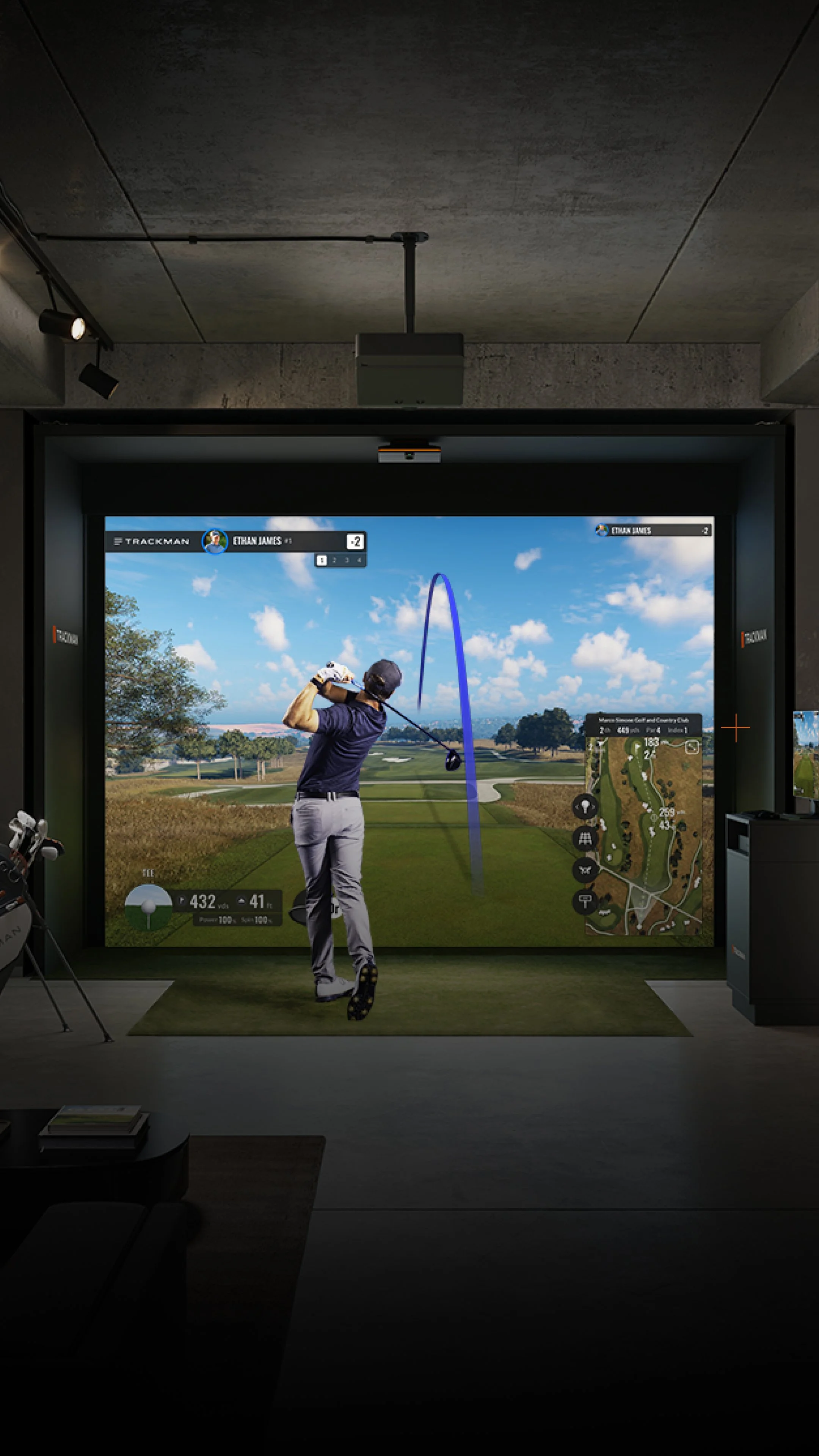Indoor golf simulation room with a large screen displaying a golf course, a man playing golf in front of the screen, and golf accessories like a golf bag and a small map on the screen.