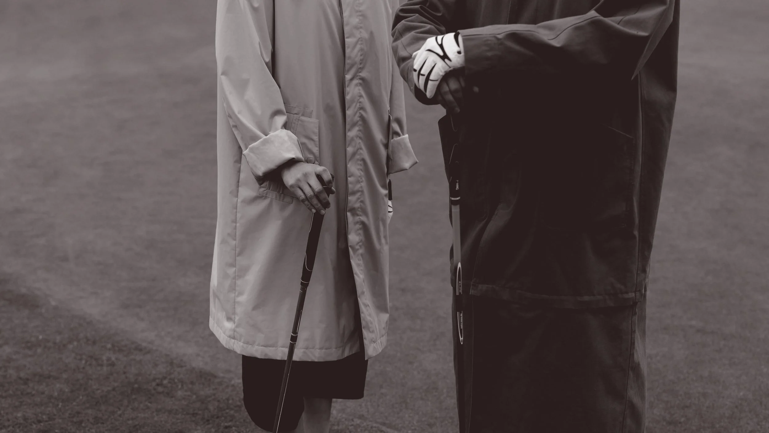Two people on a golf course, both holding golf clubs, wearing golf attire including gloves, with no visible background details.