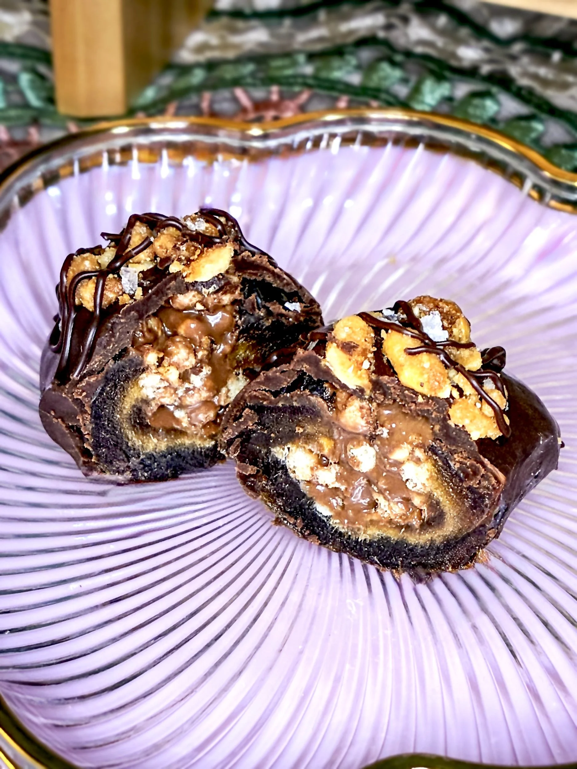 A close-up of a layered chocolate and hazelnut cocoa cream filling in a medjool date with a drizzled chocolate topping on a pink ribbed glass plate.