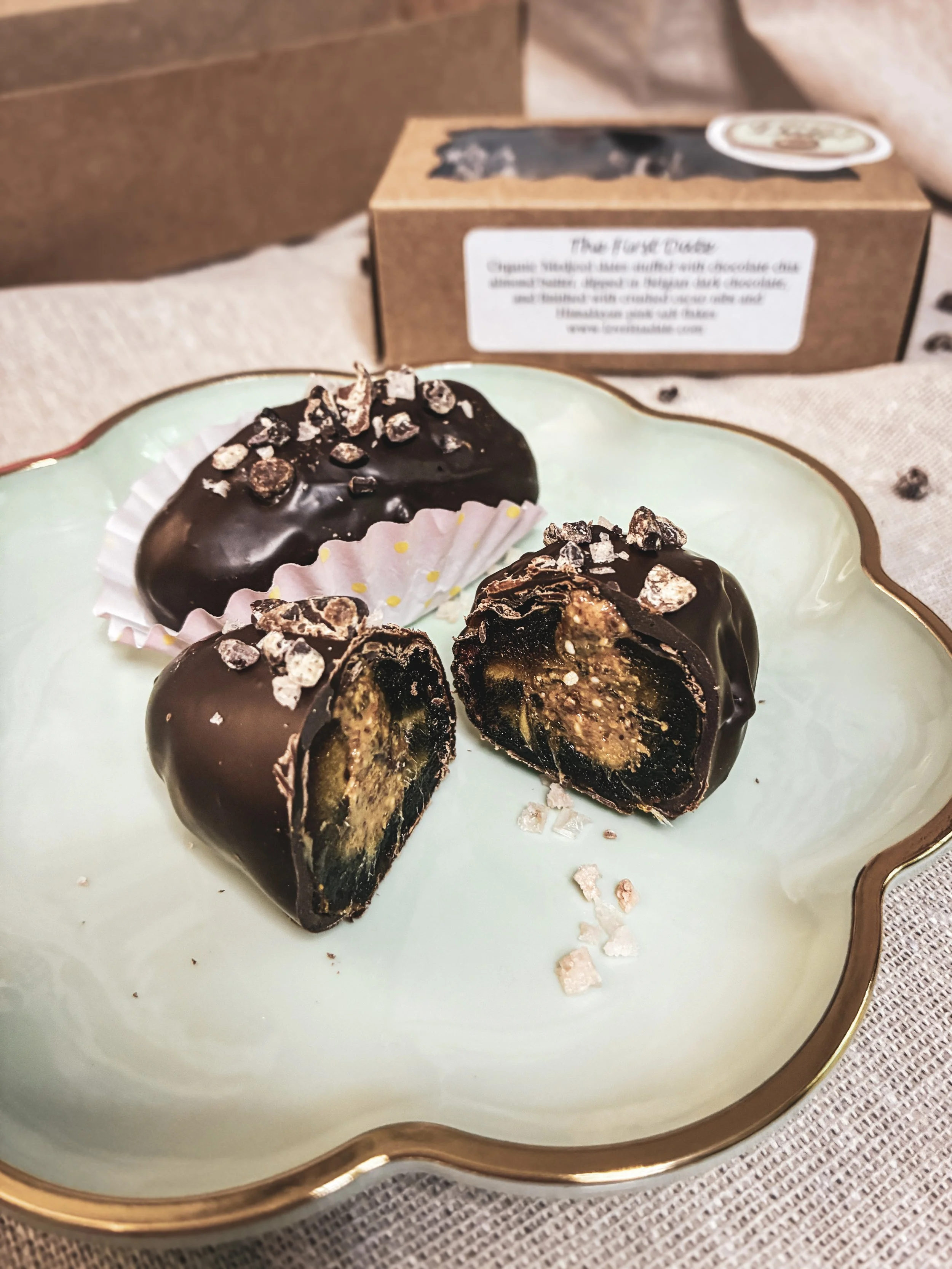 Chocolate-covered truffles on a decorative plate, with one cut in half revealing caramel, nuts, and chocolate filling inside.