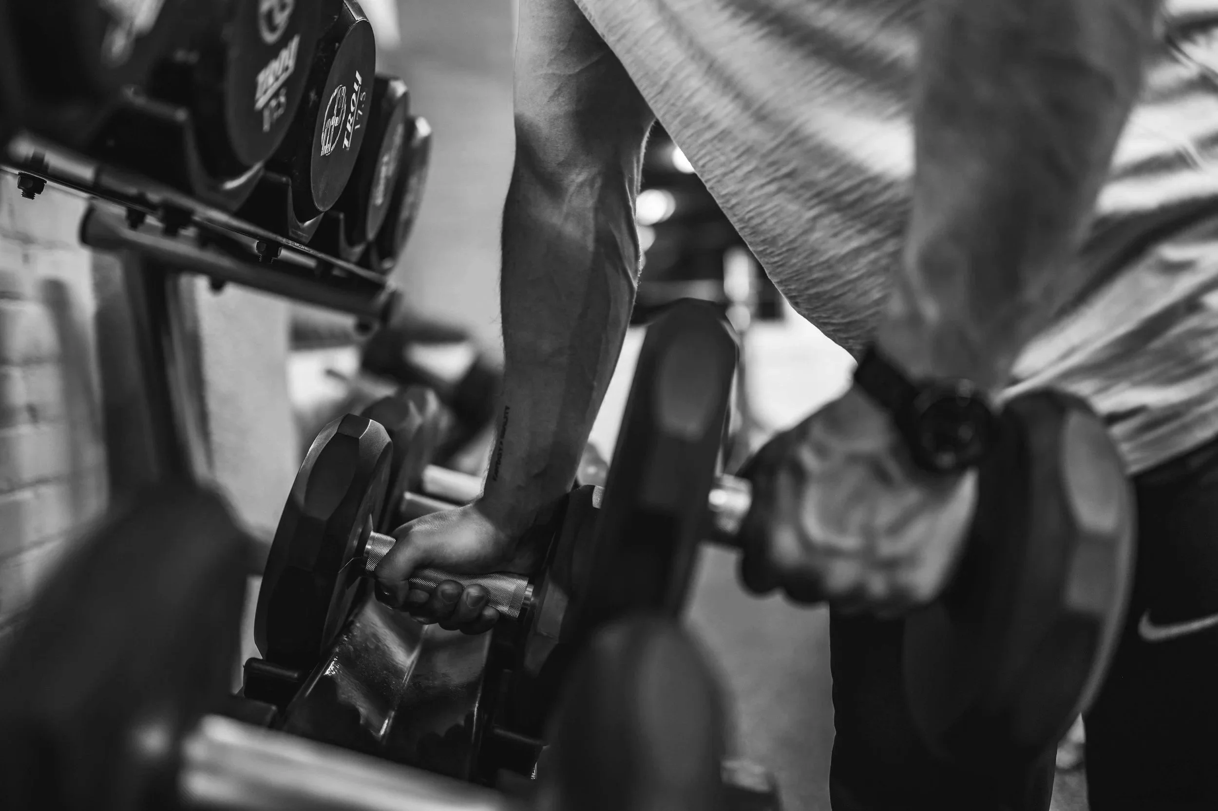 A person lifting a dumbbell in a gym, black and white photo showing their arm and the weights.