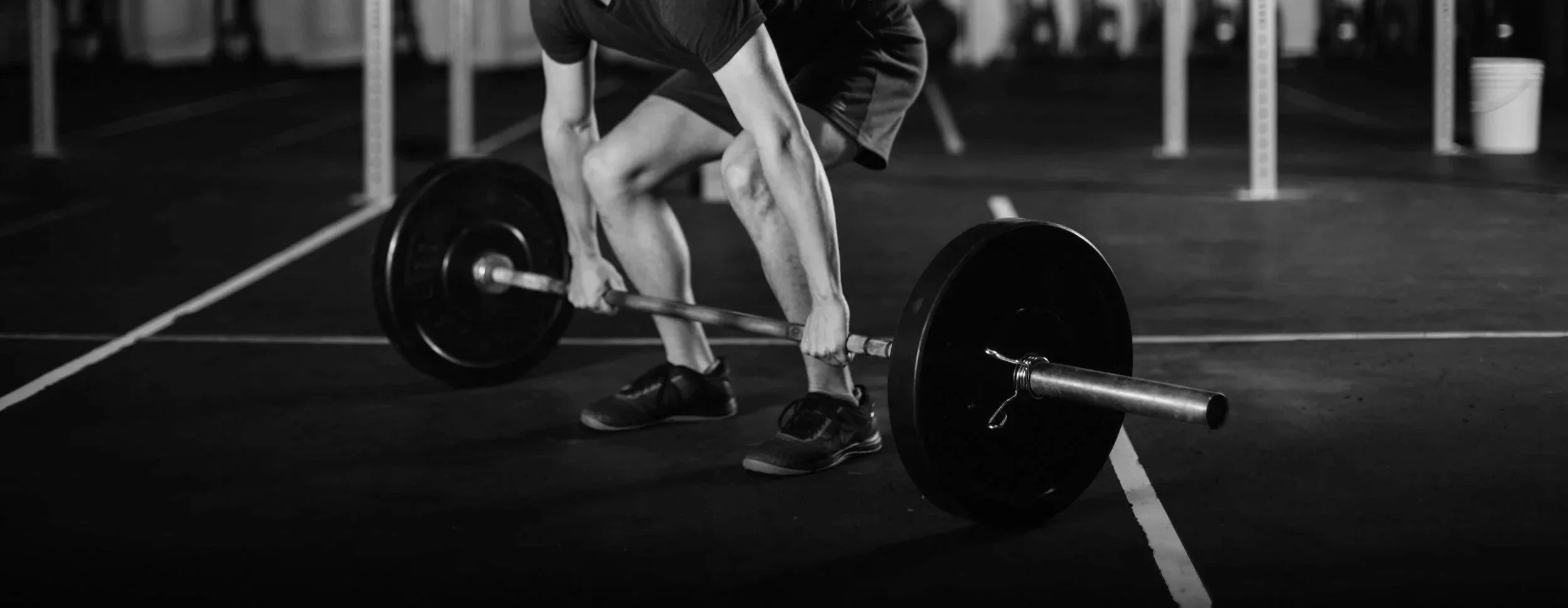 Person lifting a barbell with weights in a gym, black and white photo.