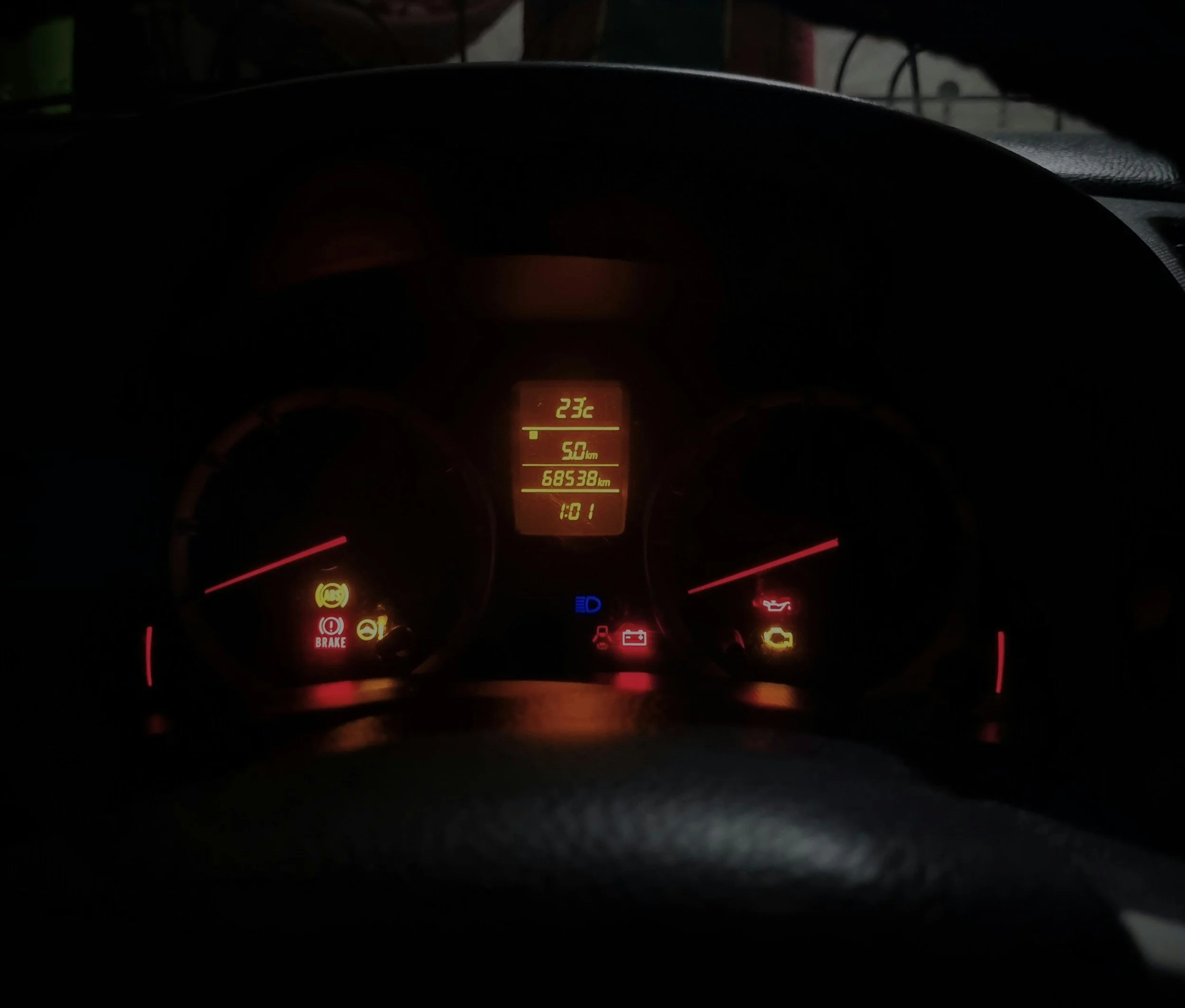 Car dashboard showing warning lights, including check engine, brake, and oil warning lights, illuminated at night.