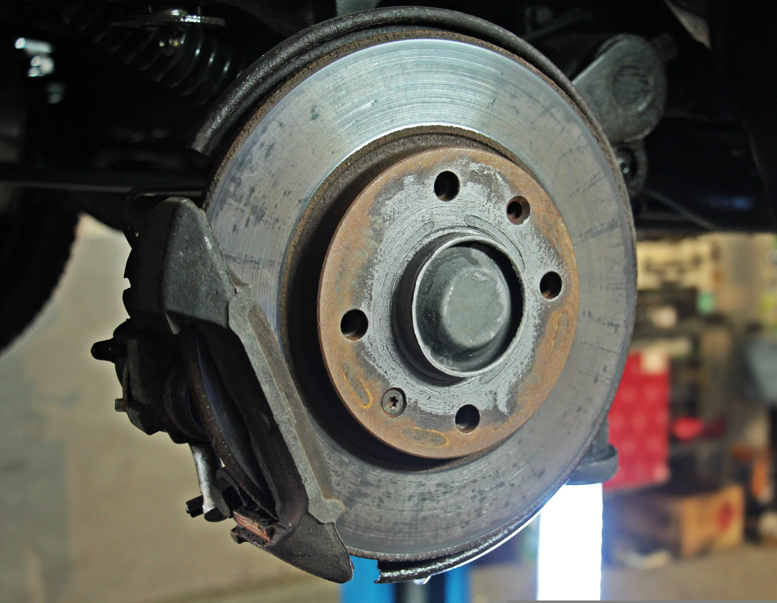 A close-up view of a metal brake disc and caliper on a vehicle, showing signs of rust and wear.