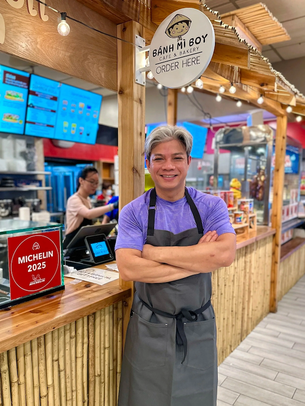 Top Chef winner Hung Huynh standing in front a 'Michelin 2025' sign at Bánh Mì Boy Café & Bakery.