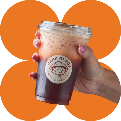 A hand holding a Thai iced tea with the Banh Mi Boy logo on an orange background.