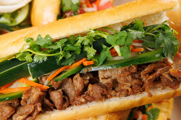 Close-up of a Banh Mi Boy Vietnamese sandwich with marinated pork, pickled vegetables, fresh cilantro, cucumber, jalapeño, and baguette bread.