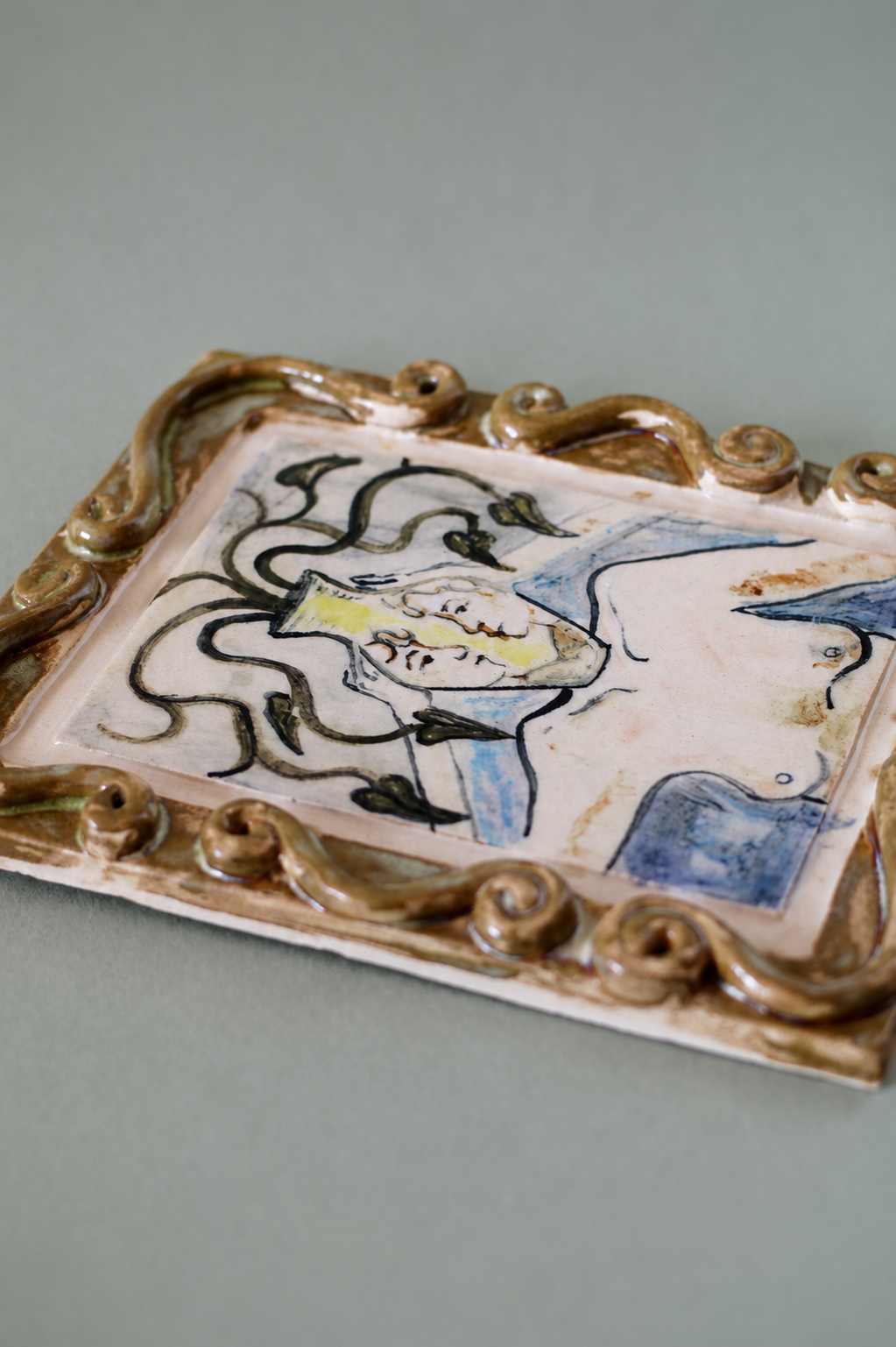 Side view of a hand-built ceramic wall piece featuring illustrated botanical forms, flowing linework and layered glazes.