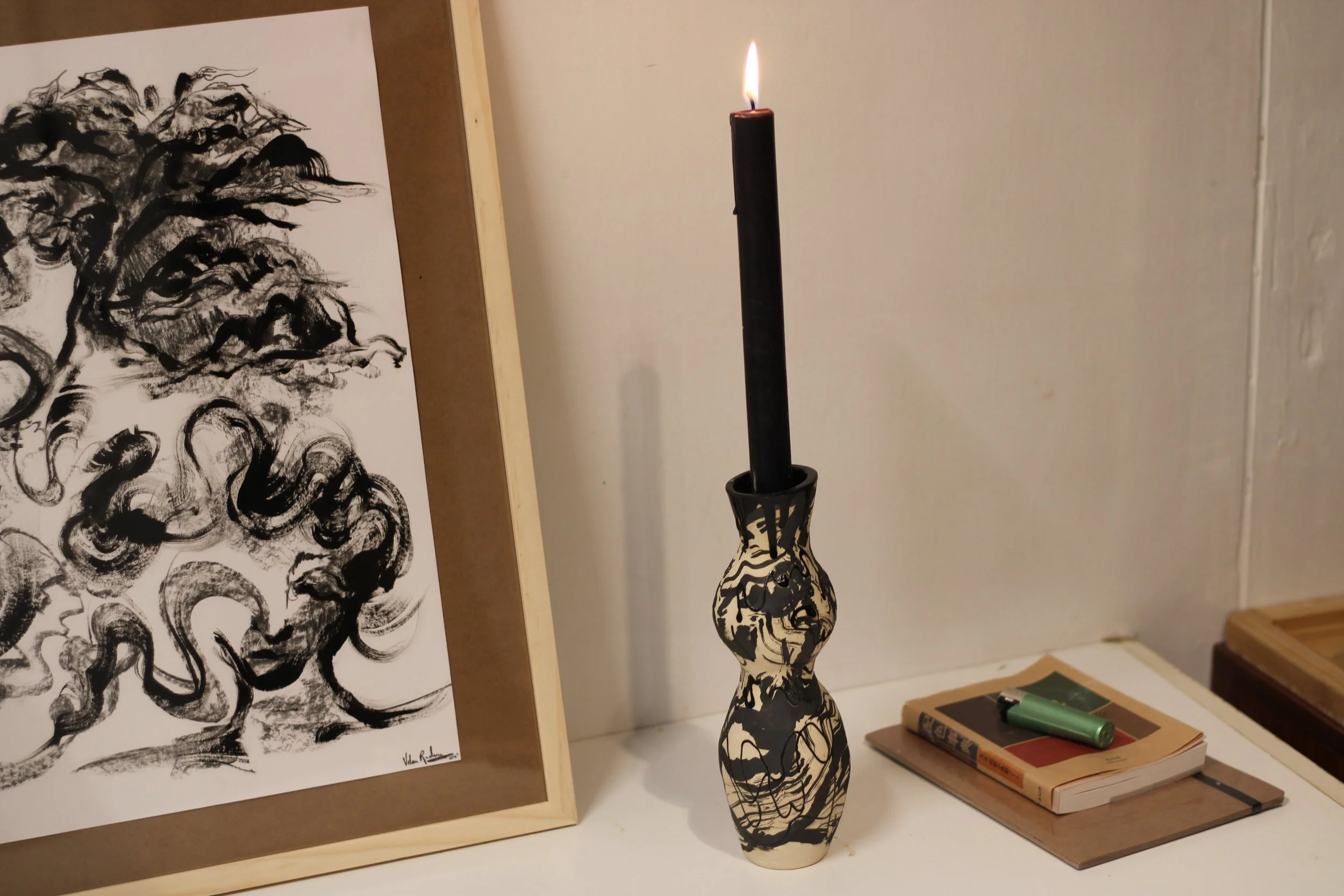 Ceramic candleholder displayed with a lit candle, featuring flowing organic forms, marbled glazes and illustrated linework