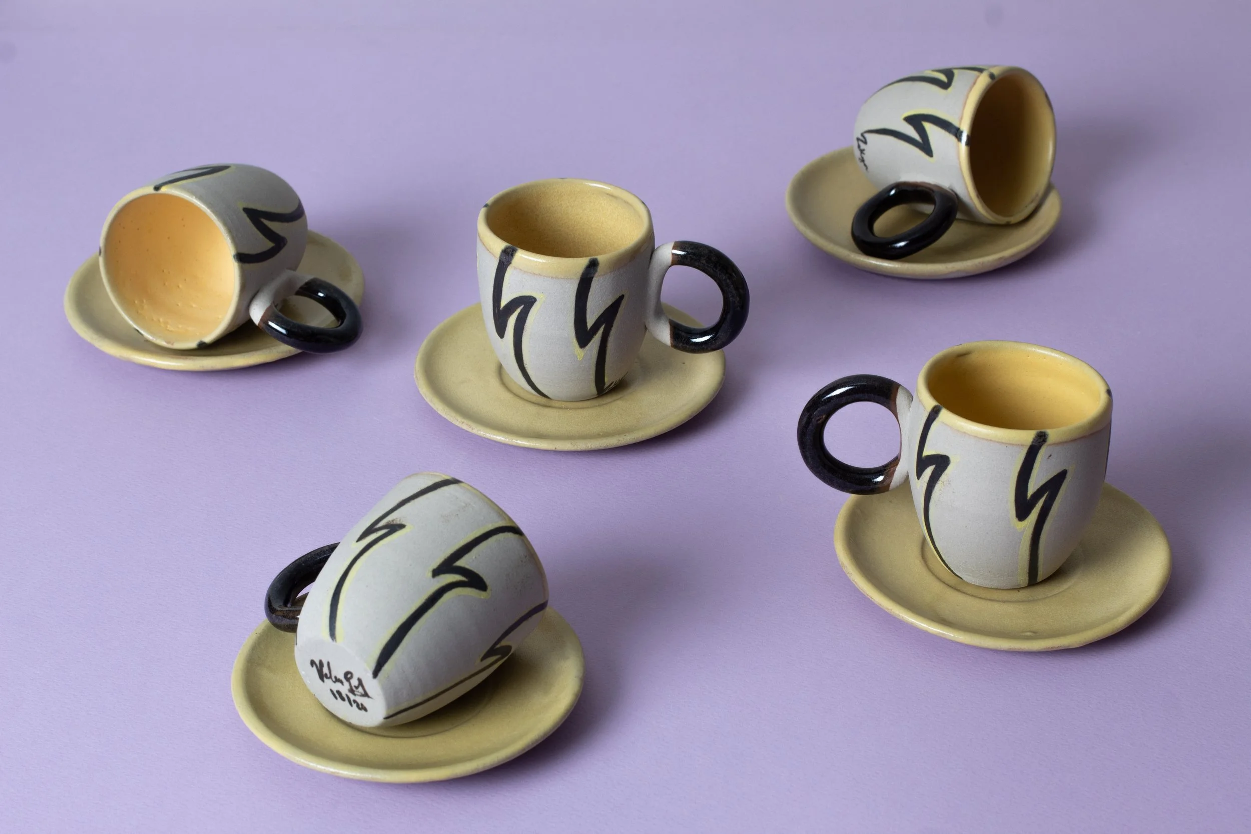 Juegos de tazas y platos con diseño colorido sobre fondo liso morado.