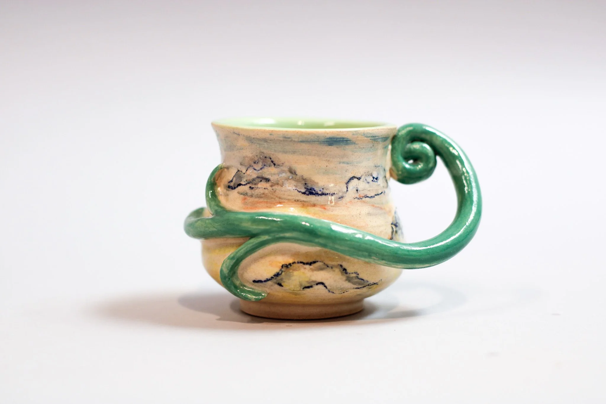 Hand-built sculptural ceramic espresso cup featuring warm sunset-toned glazes, curvy handle, and a glossy finish and an organic handcrafted form.