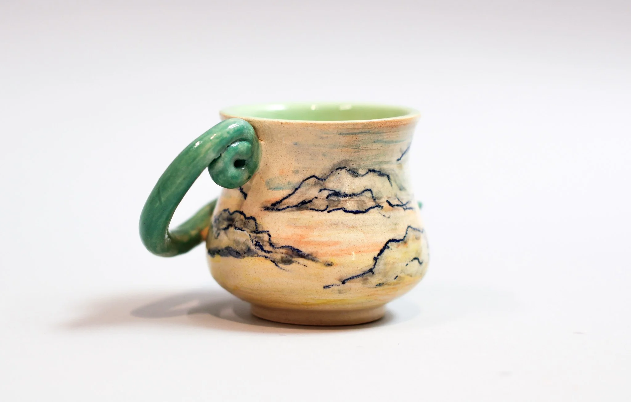 Detail of the layered sunset-toned ceramic glazes and handcrafted surface of the espresso cup.