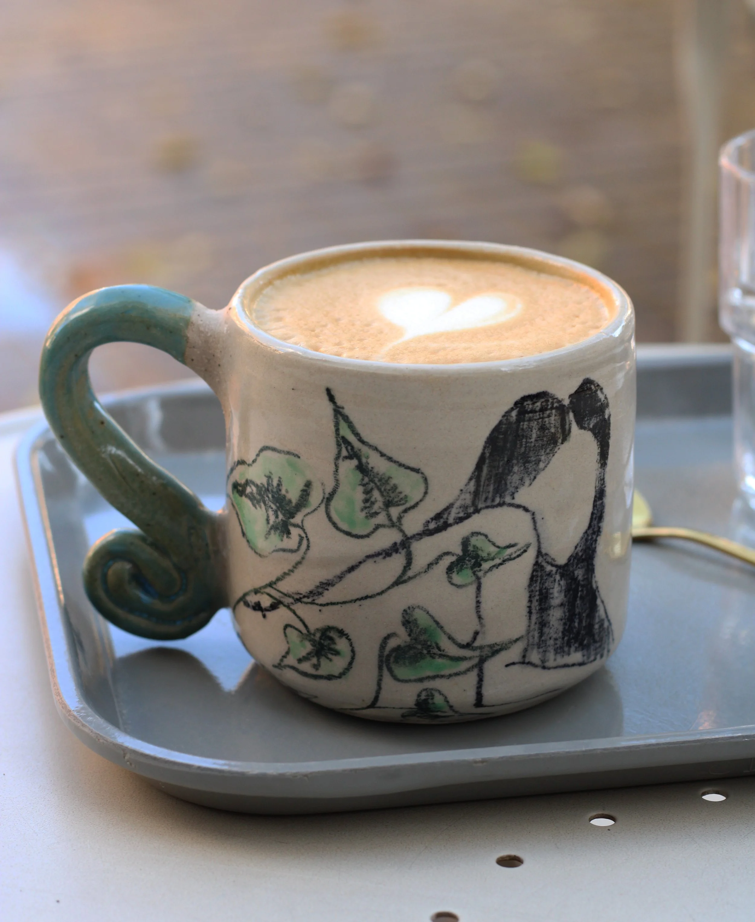 Hand-built illustrated ceramic mug featuring an original hand-drawn female figure, botanical motifs, a sculptural wave handle and layered custom ceramic glazes.