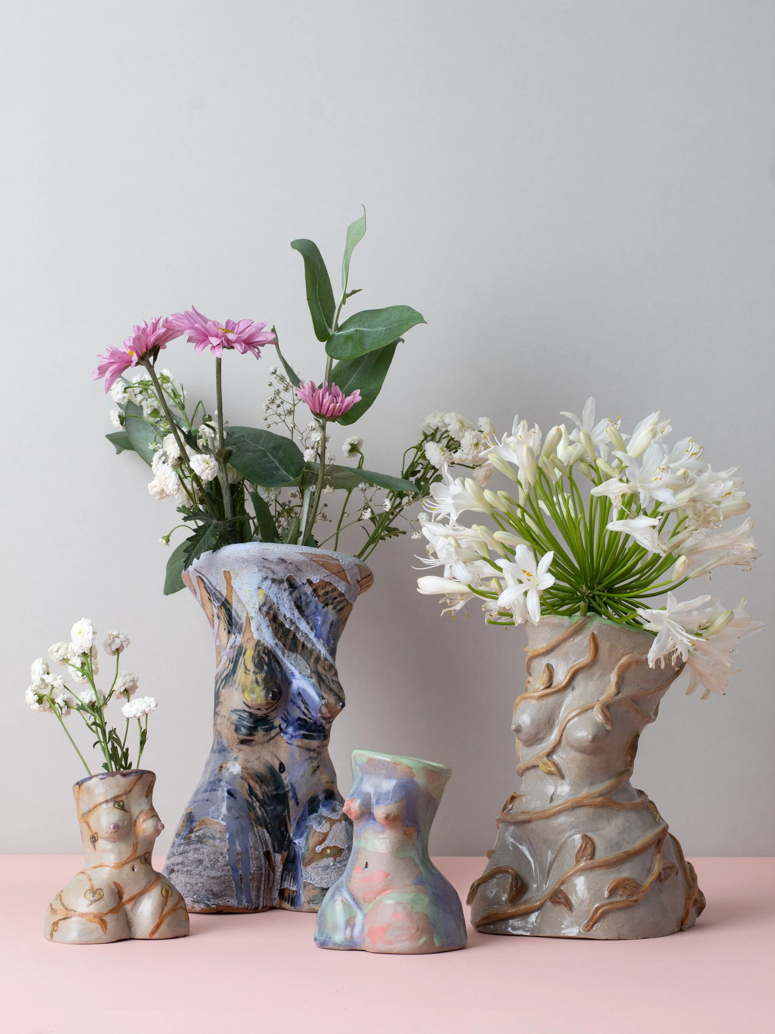 Collection of hand-built ceramic vessels inspired by the female figure, displayed with fresh flowers and featuring layered sculptural forms and handcrafted ceramic glazes.