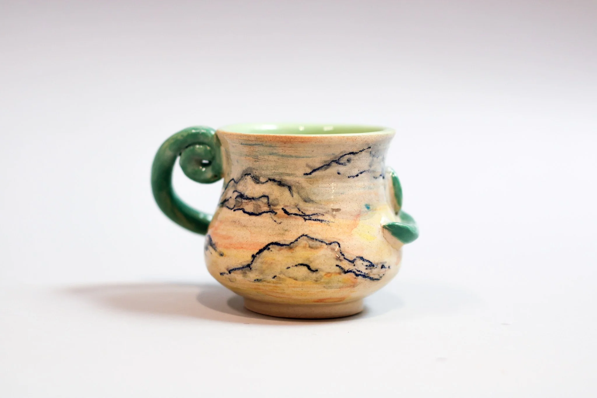 Side view of a hand-built ceramic espresso cup showing its curvy handle and glossy finish.
