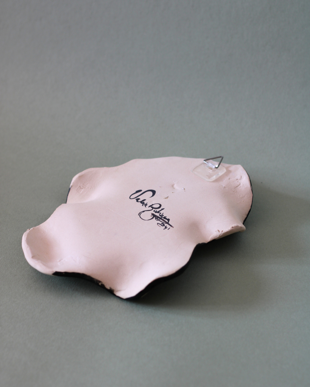 Detail of the reverse side of a hand-built illustrated ceramic plate, highlighting the artist signature