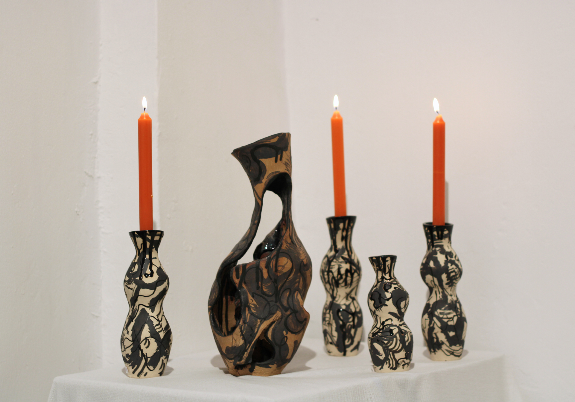 Ceramic candleholder displayed with diffrent vessels, and other candleholder flowing organic forms, marbled ceramic glazes and illustrated linework.