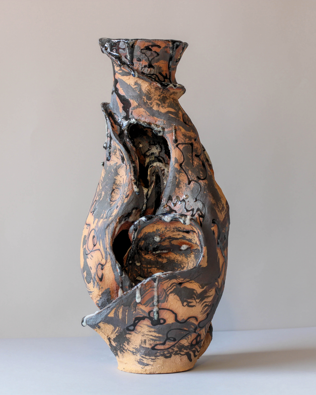 Hand-built ceramic vessel with sculptural organic openings and flowing hand-carved forms, revealing its hollow interior through an asymmetrical opening.