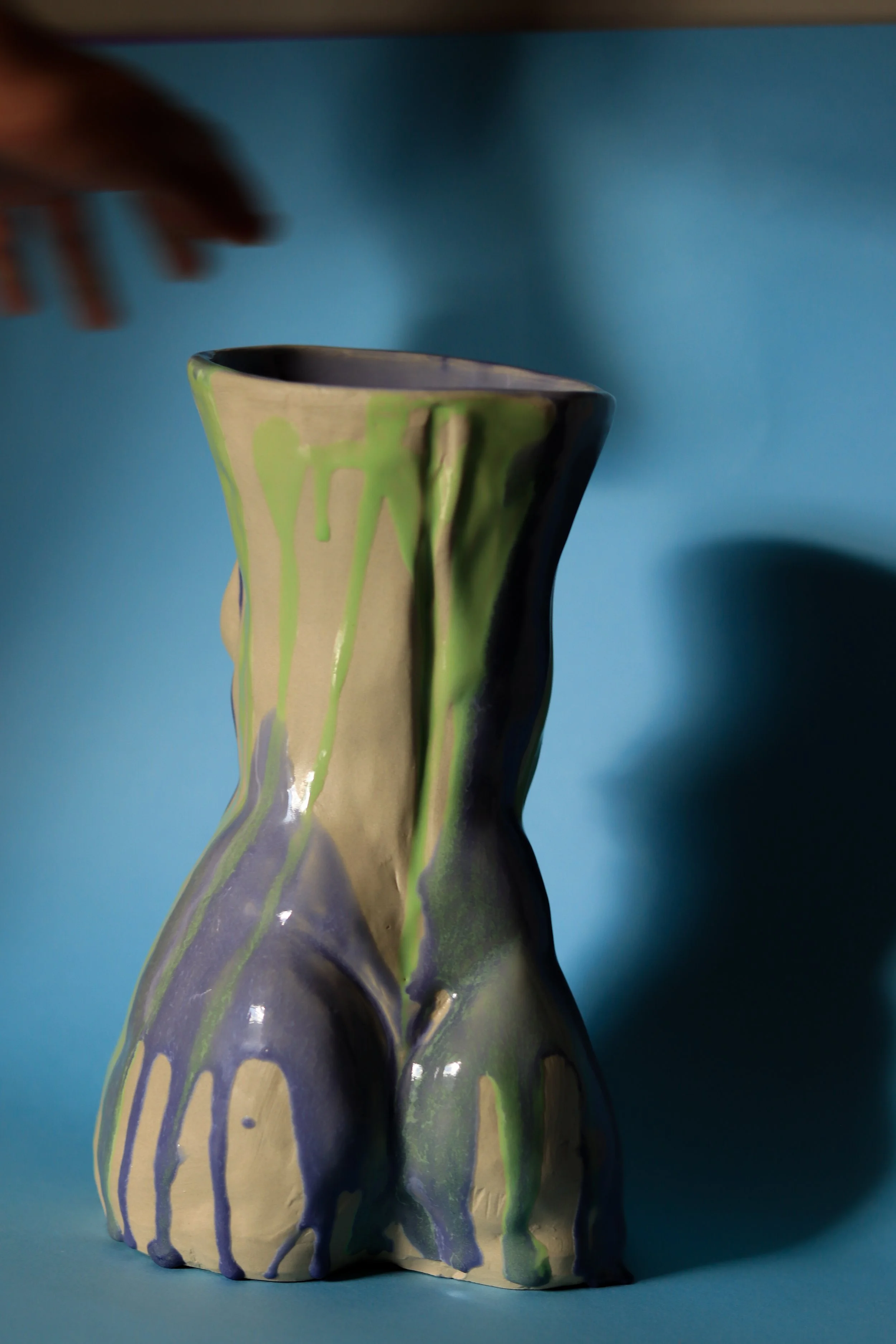 Detail of backside of the sculptural ceramic vessel inspired by the female figure, featuring expressive blue and light green dripping glazes and organic sculptural curves.
