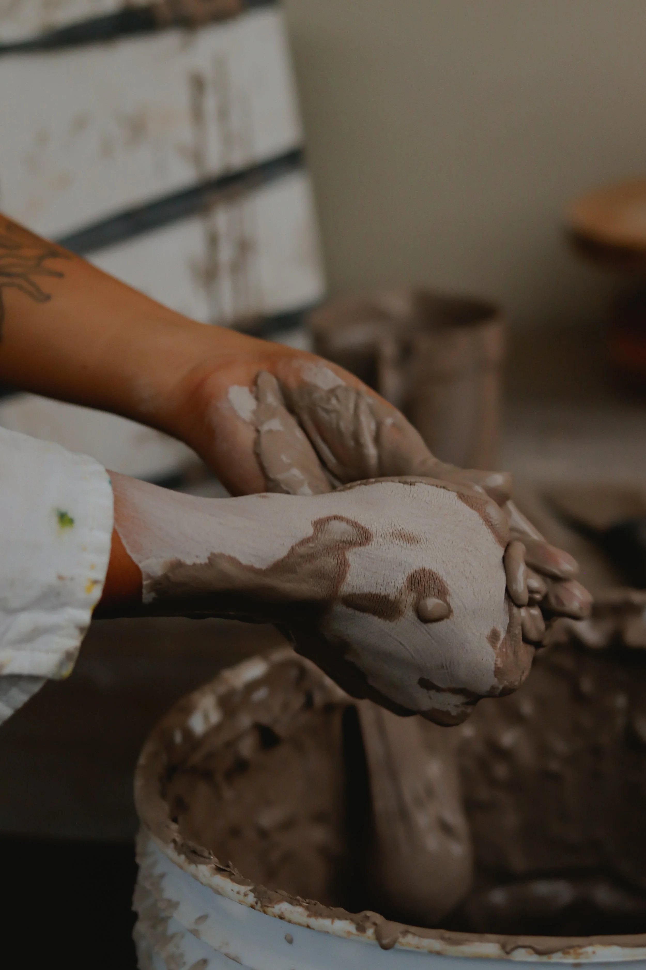 Detail of the artist’s hands shaping clay in the ceramic atelier during the hand-building process.
