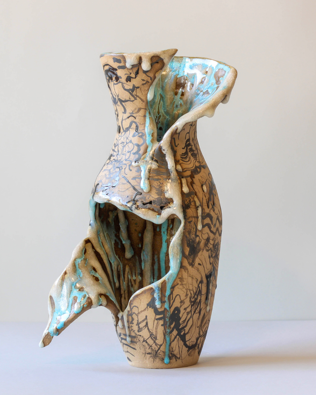 Hand-built ceramic vessel with an opened sculptural form, revealing its interior through carved organic openings and personally formulated ceramic glazes.