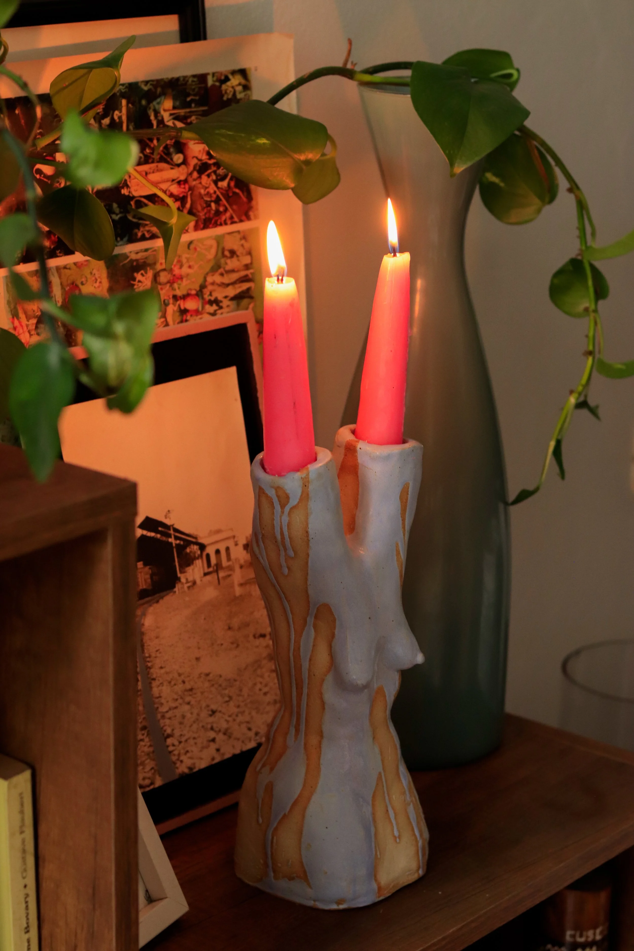 Sculptural ceramic candleholder shaped as a female figure, dripped with paint, holding two lit candles and displayed in the living space of a private collector.