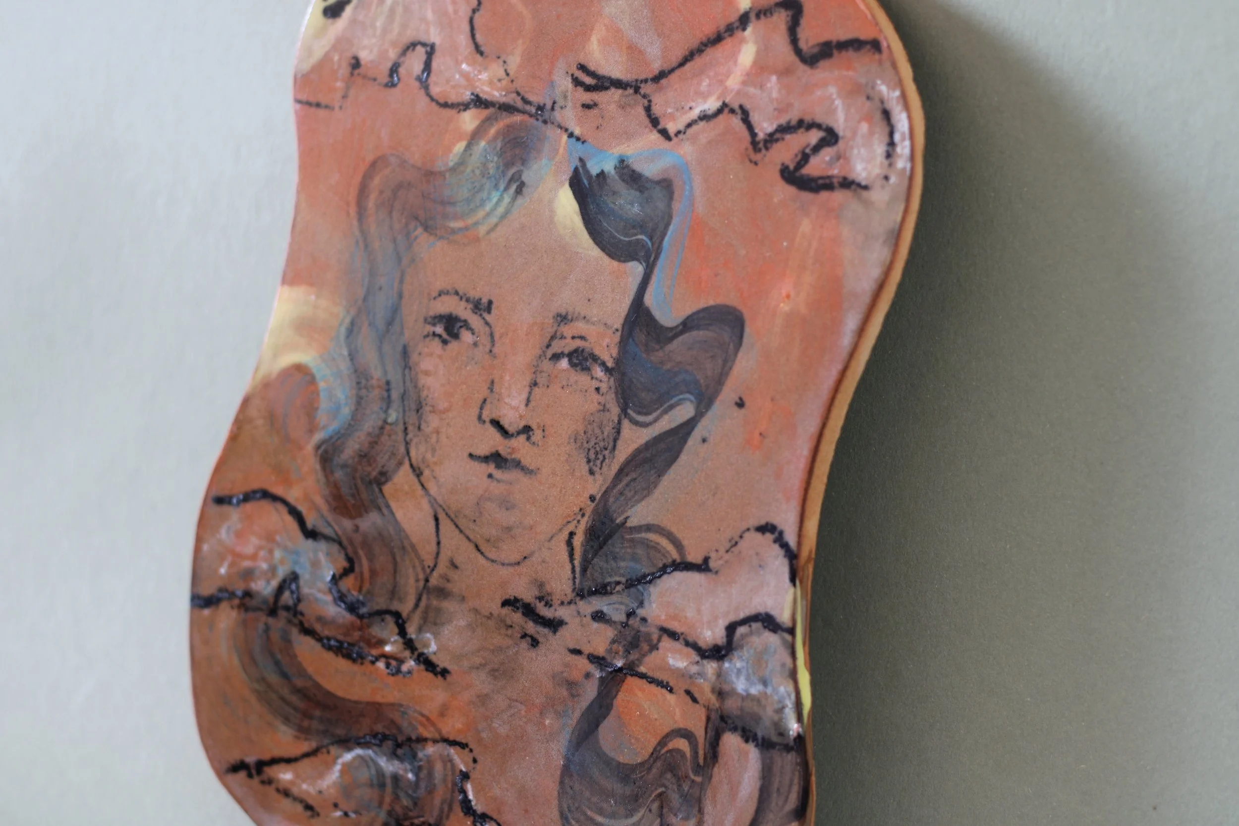 Detail of ceramic wall piece displayed in an interior, featuring a painted portrait surrounded by swirling pastel-colored glazes on a reddish-brown clay surface
