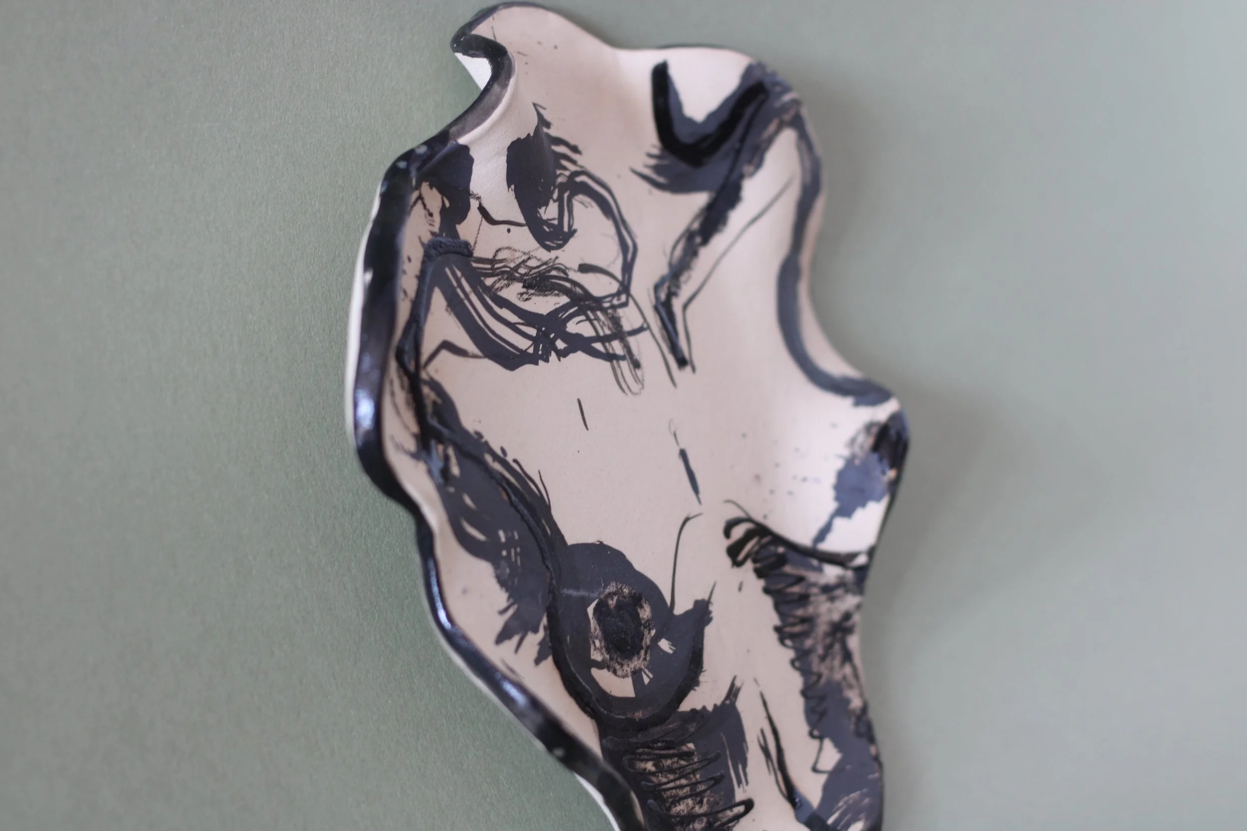 Side view of a hand-built illustrated ceramic plate featuring an abstract body motif, flowing linework and marbled glazes.