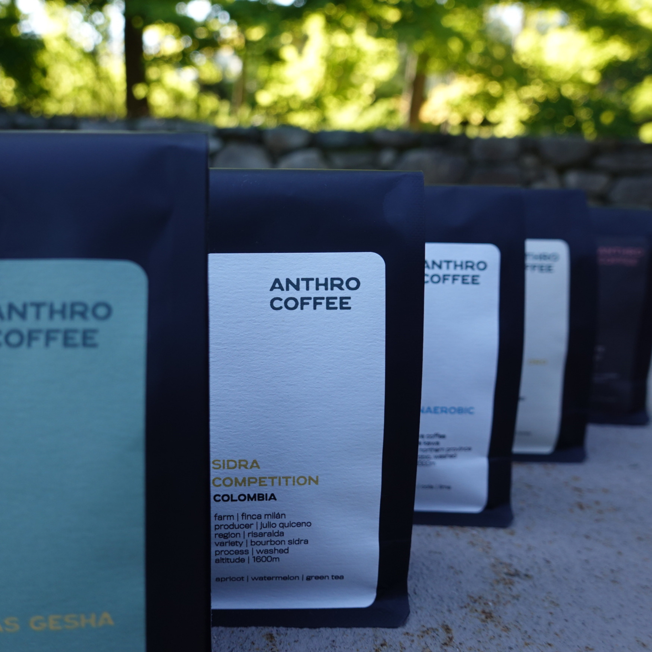 Close-up of labels on coffee bags outdoors, with a stone wall and green foliage in the background.