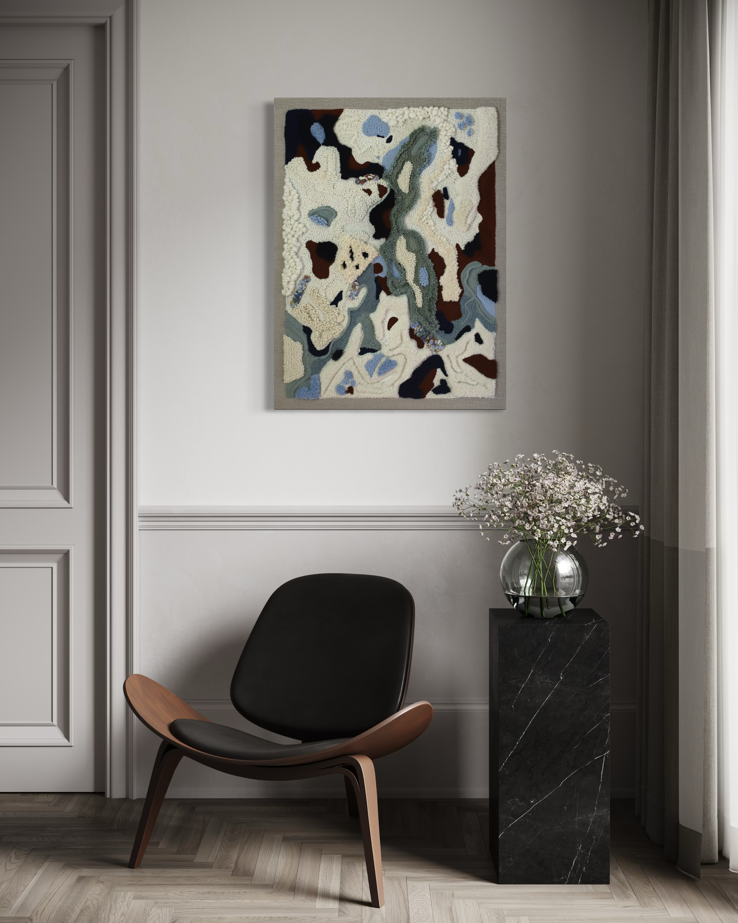A modern interior with a black and wood lounge chair, a vase of pink flowers on a black marble stand, and an abstract textured wall art hanging on a gray wall.