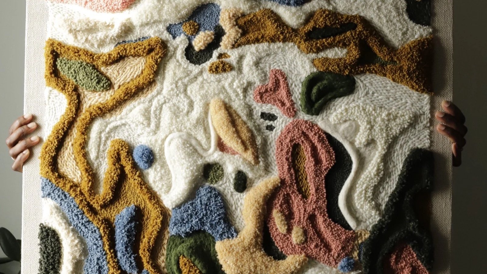 A textured abstract art piece made of multicolored raised yarns on a neutral background, with various shapes and patterns.
