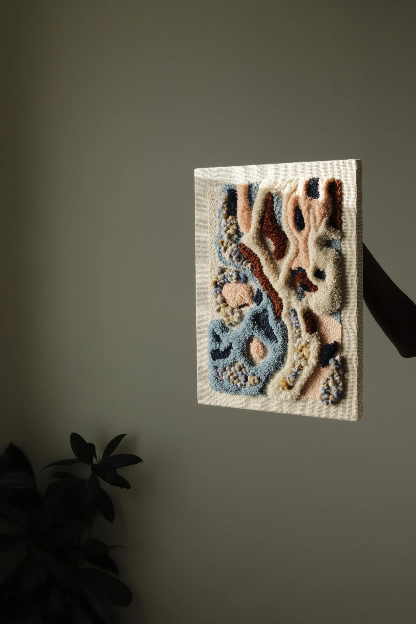 Textured abstract art piece with swirls and raised patterns in pastel colors mounted on a wall with a shadow cast to the right.