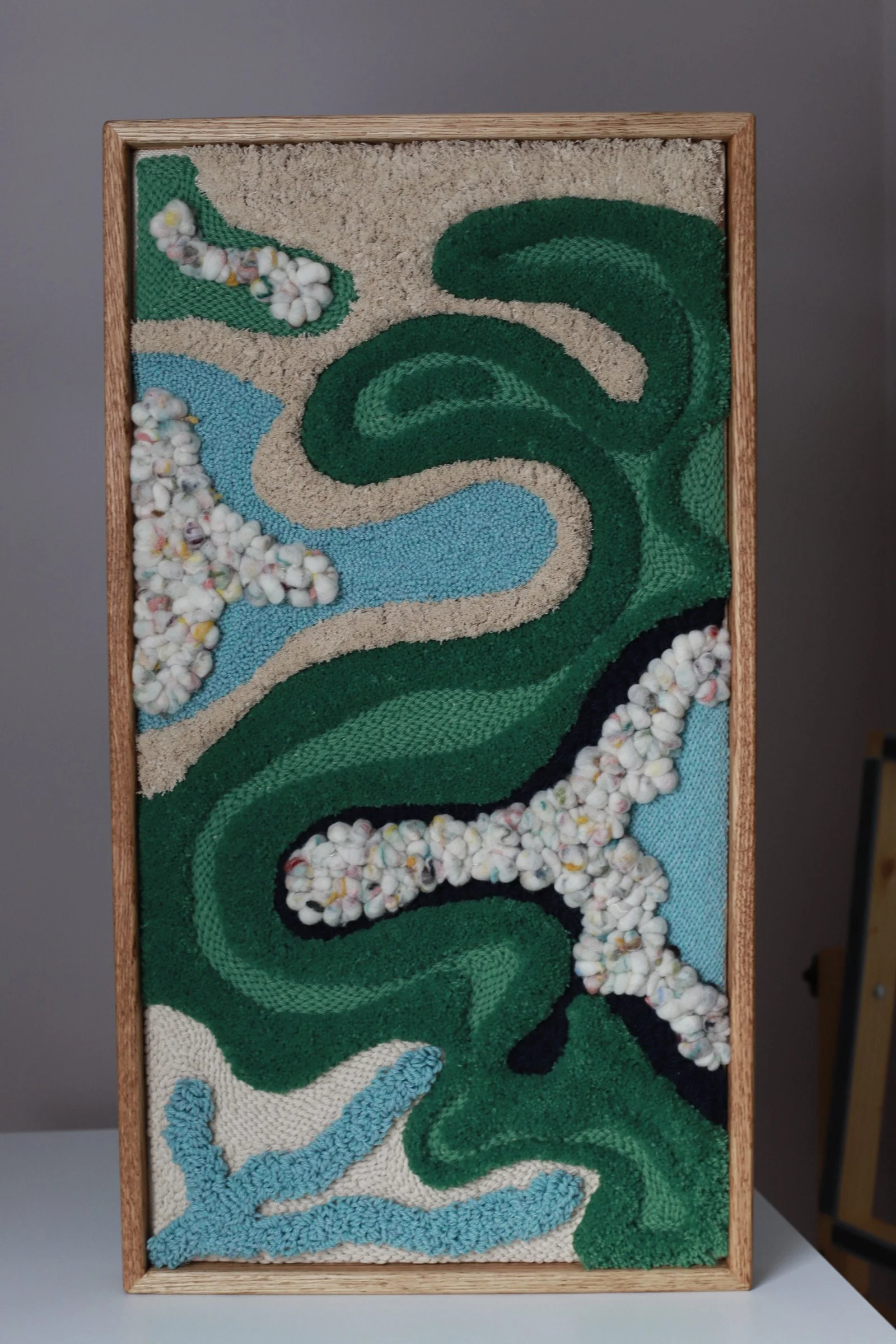 Textured wall art with swirling green and blue patterns, beige and black accents, bordered by a light wooden frame.