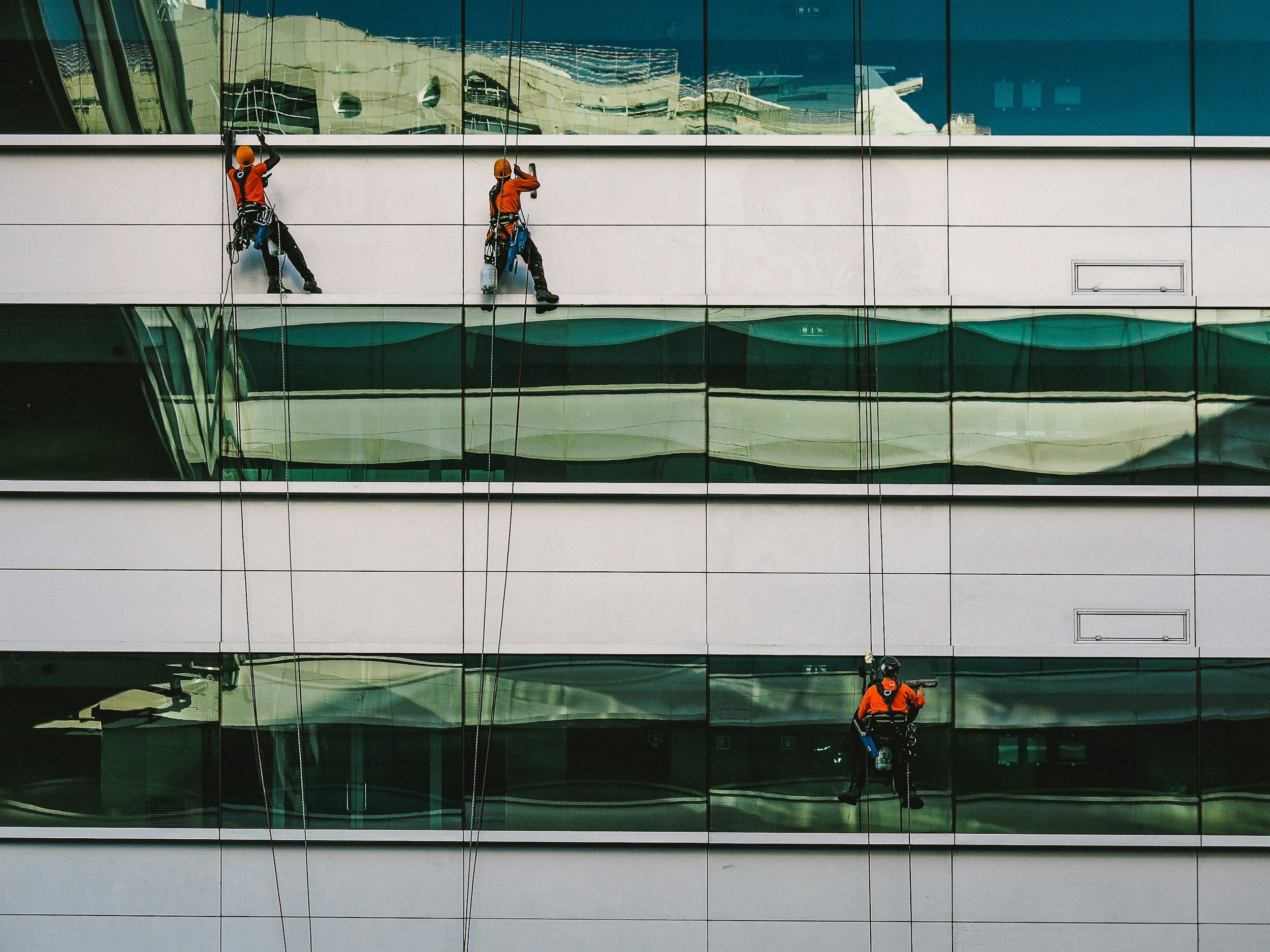 window cleaning on a several story building, men are hanging from safety ropes and using squeegee and sponge to create spotless windows.