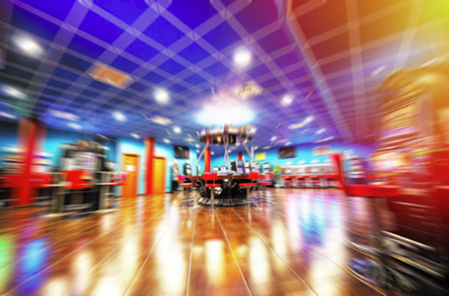 Blurred image of an indoor arcade with various game stations and bright colorful ceiling lights.
