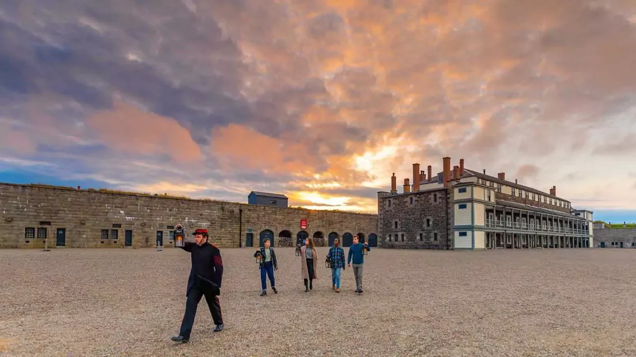 Group of tourists walking outside of historic fort with stone walls and large building at sunset.