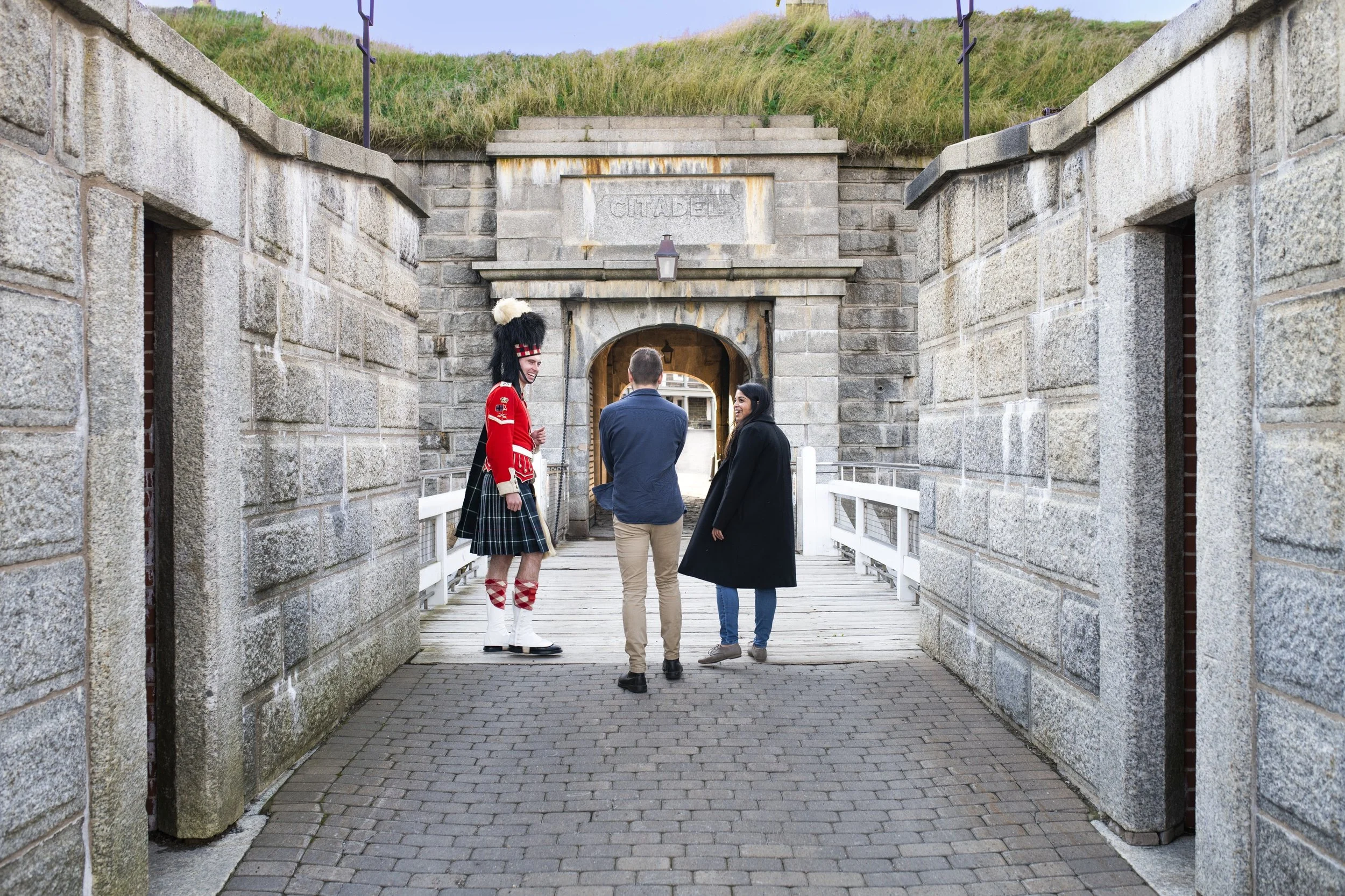 Three people, including one dressed in a 78th Highlander uniform, are standing and talking beneath the Citadel archway at Portsmouth Historic Dockyard.