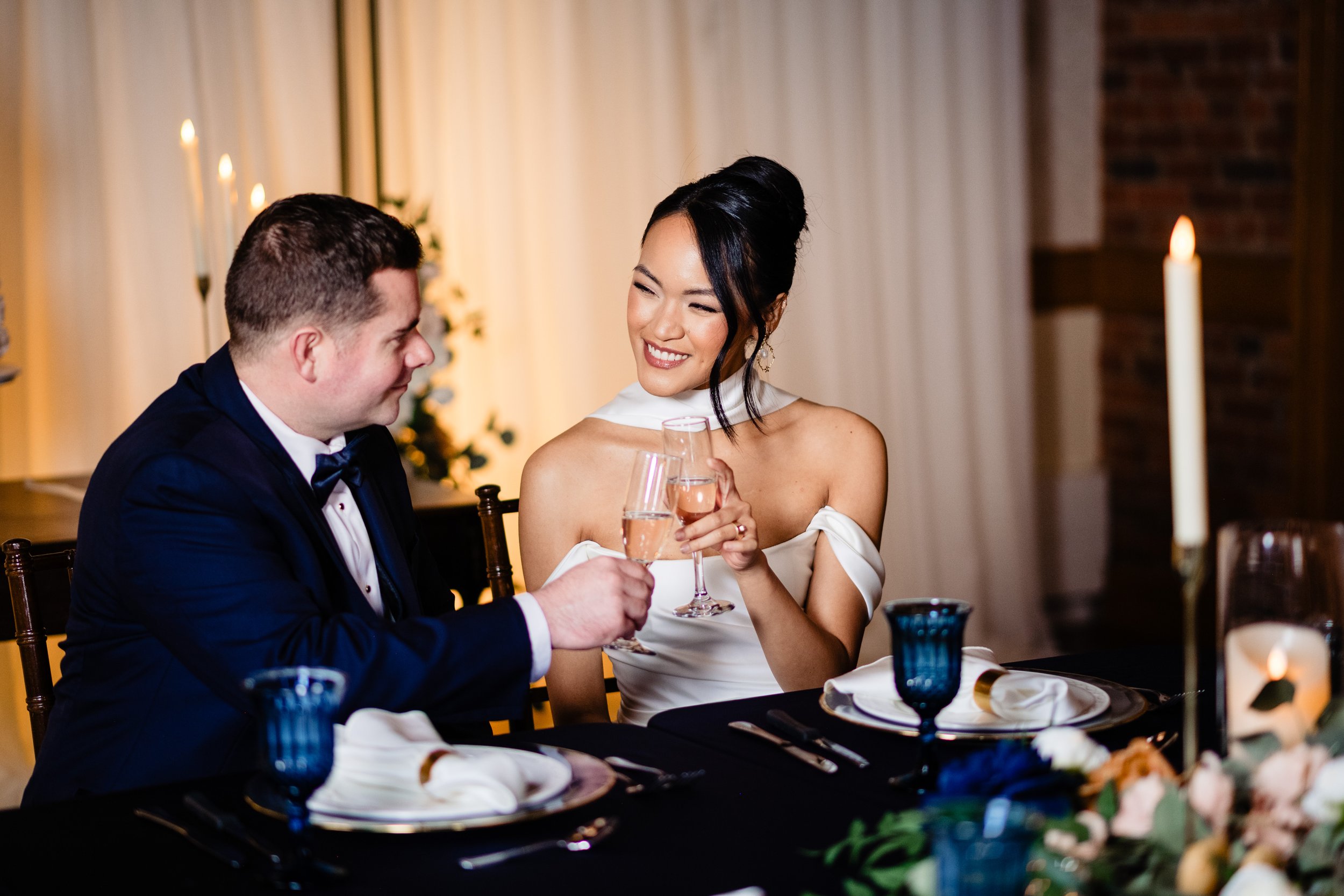 A woman and man in formal attire at a dinner table, smiling and clinking champagne glasses during a celebration.