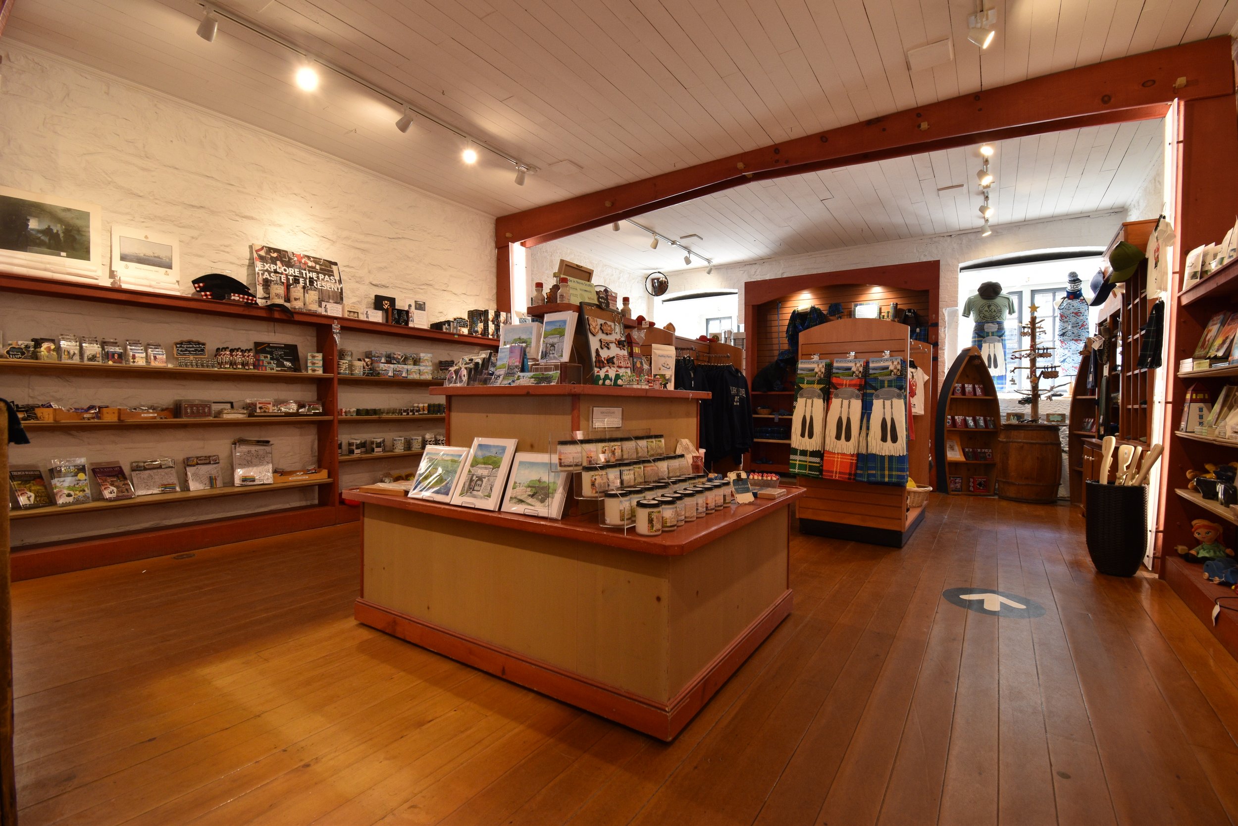 Interior of the Regimental Shop, a gift shop with wooden shelves, artwork, apparel, and various merchandise displayed, with large windows in the background letting in natural light.