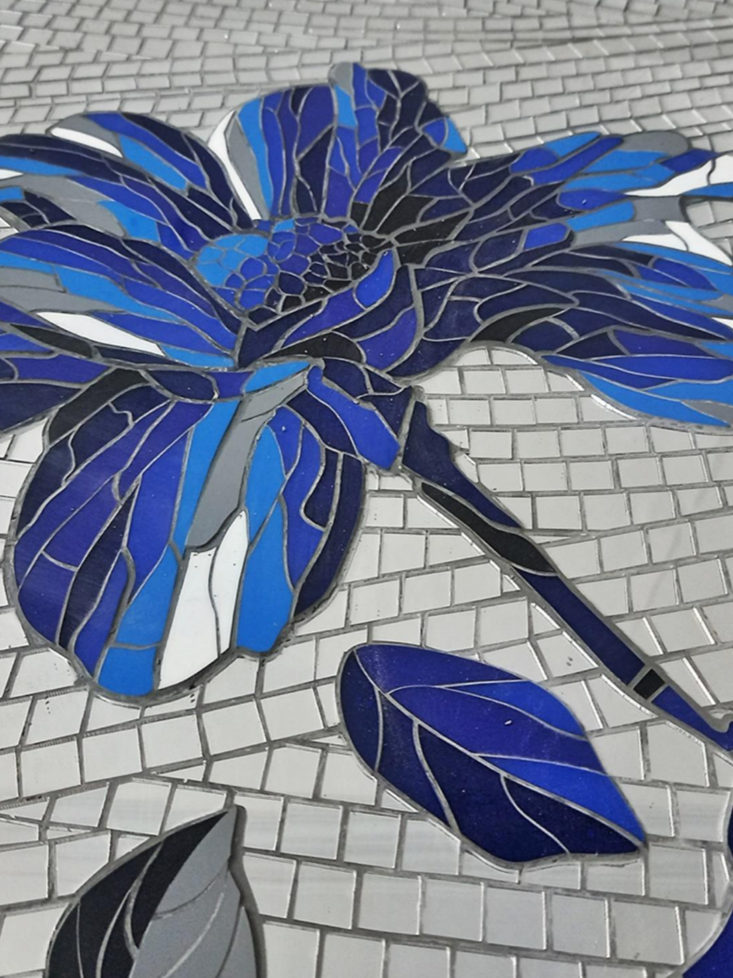 Blue and black mosaic art of a rose with leaves on a tiled pavement.