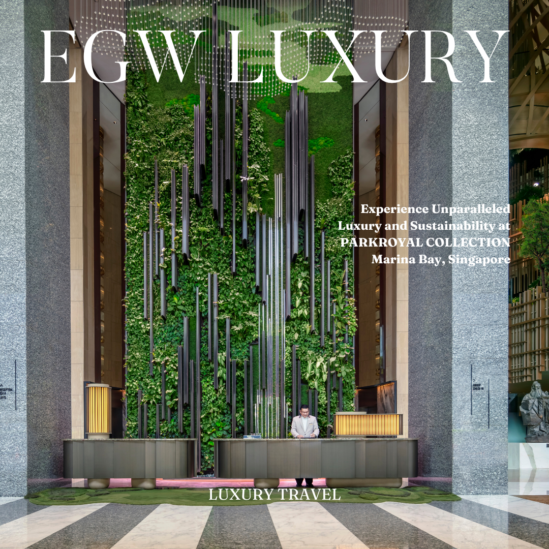 A hotel lobby with a green living wall behind a modern reception desk, featuring a man standing at the desk. The lobby has gray stone walls and a polished floor, with a sculpture visible on the right. The image is overlaid with text promoting luxury 